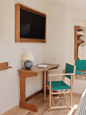 Une pièce comprenant un bureau en bois, une chaise, une lampe, un téléviseur et un portant à vêtements.