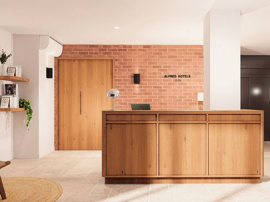Un mostrador de recepción con detalles de madera, una pared de ladrillo y un cartel que dice 'ALFRED HOTELS'.