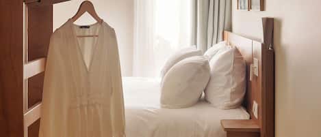 Un dormitorio con cama, perchero, mesita de noche de madera y ventana con cortinas.