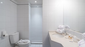 Une salle de bain moderne avec des carreaux blancs, des toilettes, un lavabo avec un miroir et des serviettes.