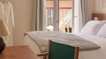 Une chambre d’hôtel comprenant un lit, un bureau, une chaise, une fenêtre avec des rideaux et une vue sur un bâtiment doté d’un toit en tuiles.