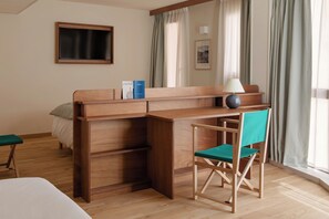 Ein Hotelzimmer mit einem Holztisch, einem grünen Stuhl, einem Bett, einem kleinen Tisch und einem Fenster mit Vorhängen.