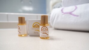 Trois bouteilles de gel douche pour les cheveux et le corps sont posées sur un comptoir, avec une serviette et une enseigne d’hôtel en arrière-plan.