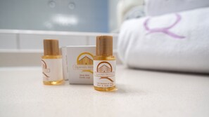 Trois bouteilles de gel douche pour les cheveux et le corps sont posées sur un comptoir, avec une serviette et une enseigne d’hôtel en arrière-plan.