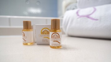 Tres botellas de jabón para cabello y cuerpo sobre una encimera, con una toalla y un cartel de hotel al fondo.