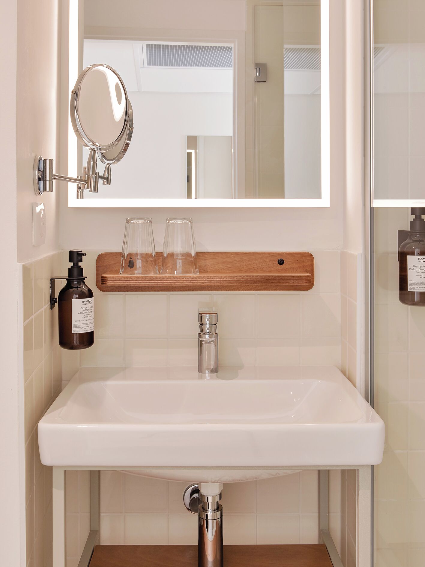 A bathroom with a white sink, a mirror, a soap dispenser, and a glass shower enclosure.