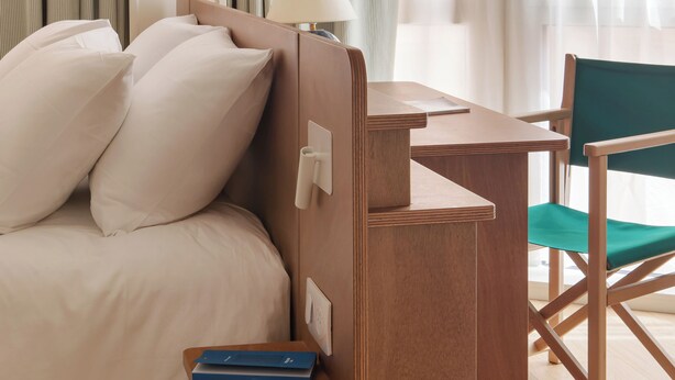 Une chambre à coucher avec un lit, une table de chevet, une lampe, une chaise et une petite étagère en bois avec des livres.