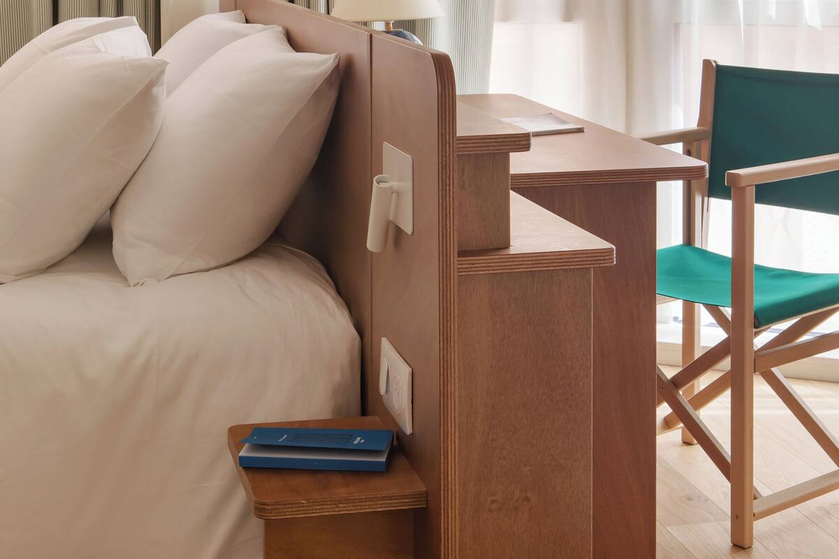 Une chambre à coucher avec un lit, une table de chevet, une lampe, une chaise et une petite étagère en bois avec des livres.
