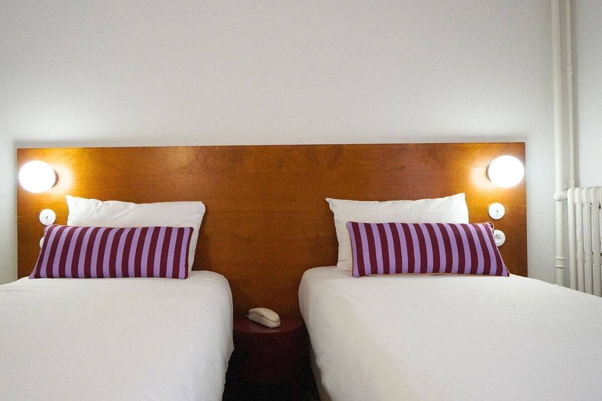 Une chambre d’hôtel avec deux lits simples, une tête de lit en bois et des lampes de chevet.