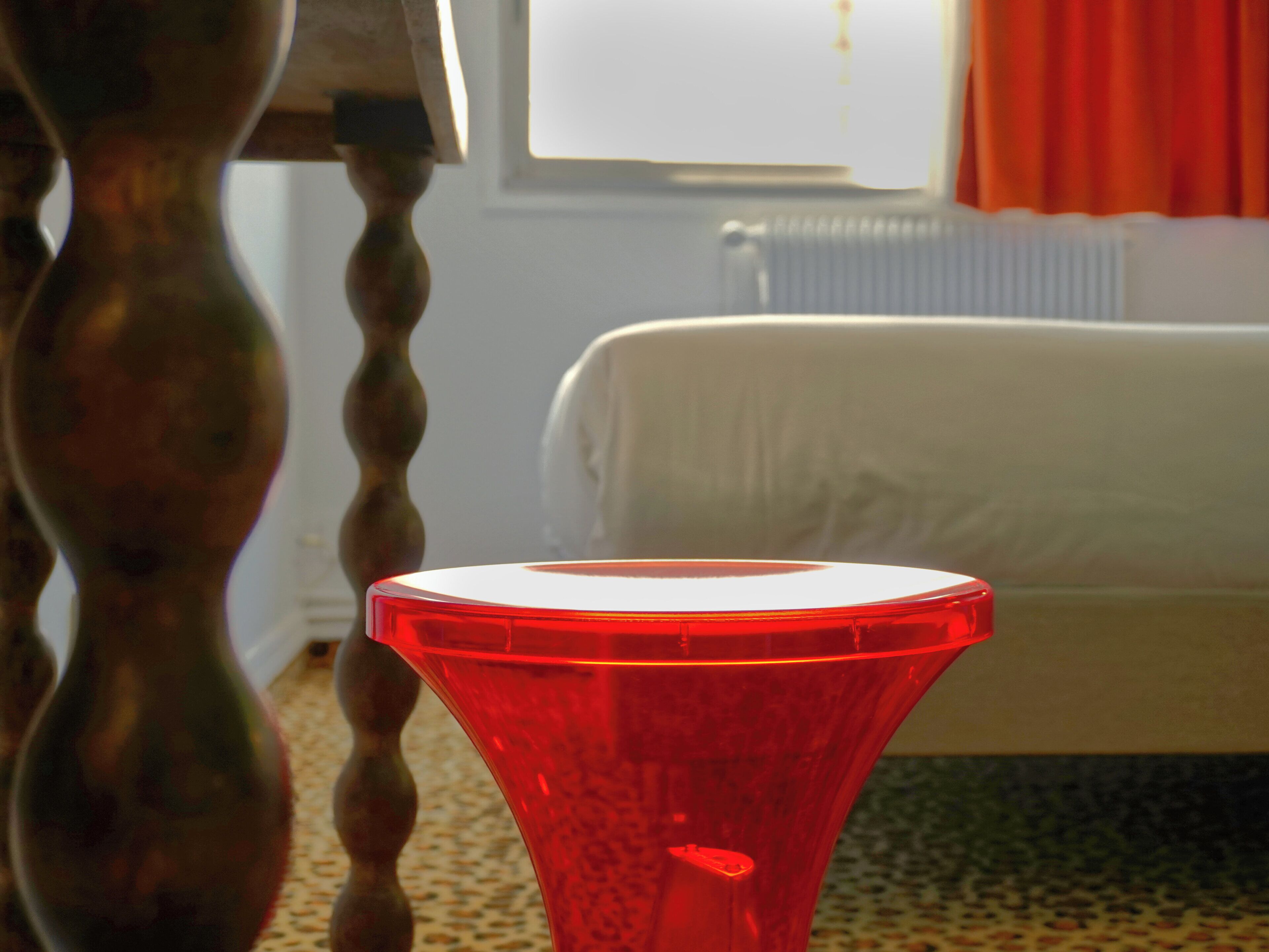 A room with a bed, a radiator, and a red object in the foreground.