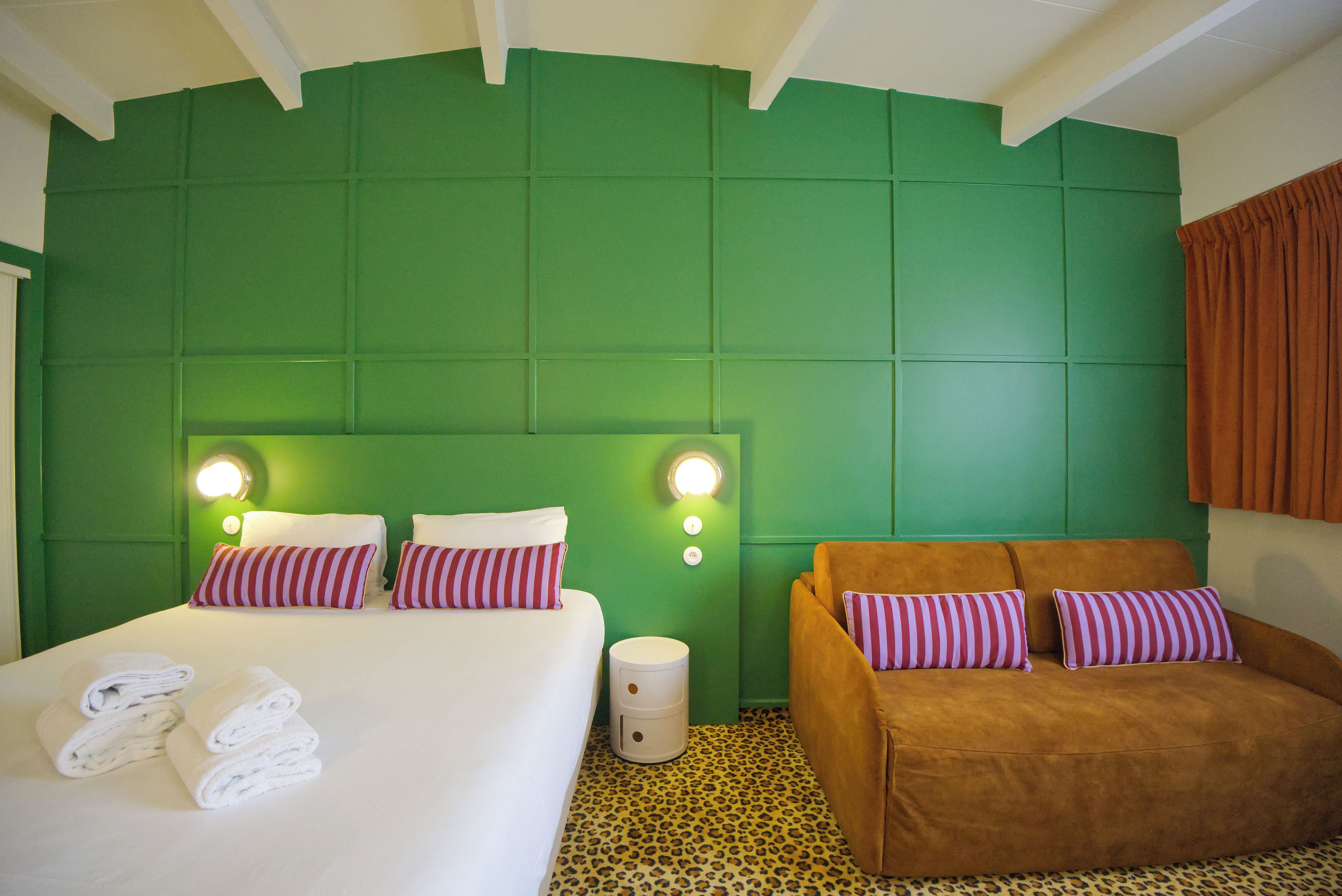 Una habitación de hotel con cama, sofá, paredes verdes y suelo estampado de leopardo.