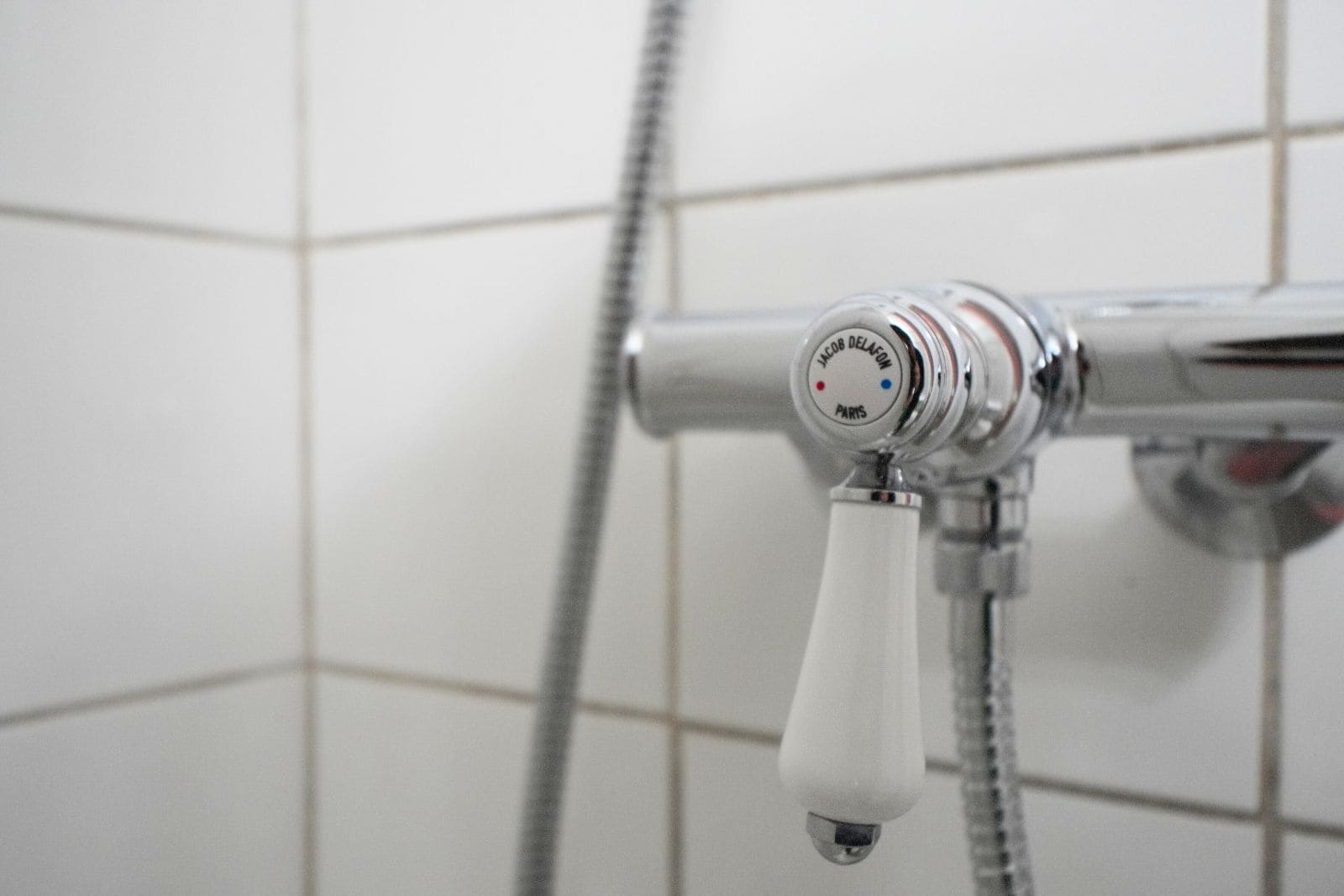 A shower head with a white handle and a control knob with 'JACOB DELAFON PARIS' engraved on it.