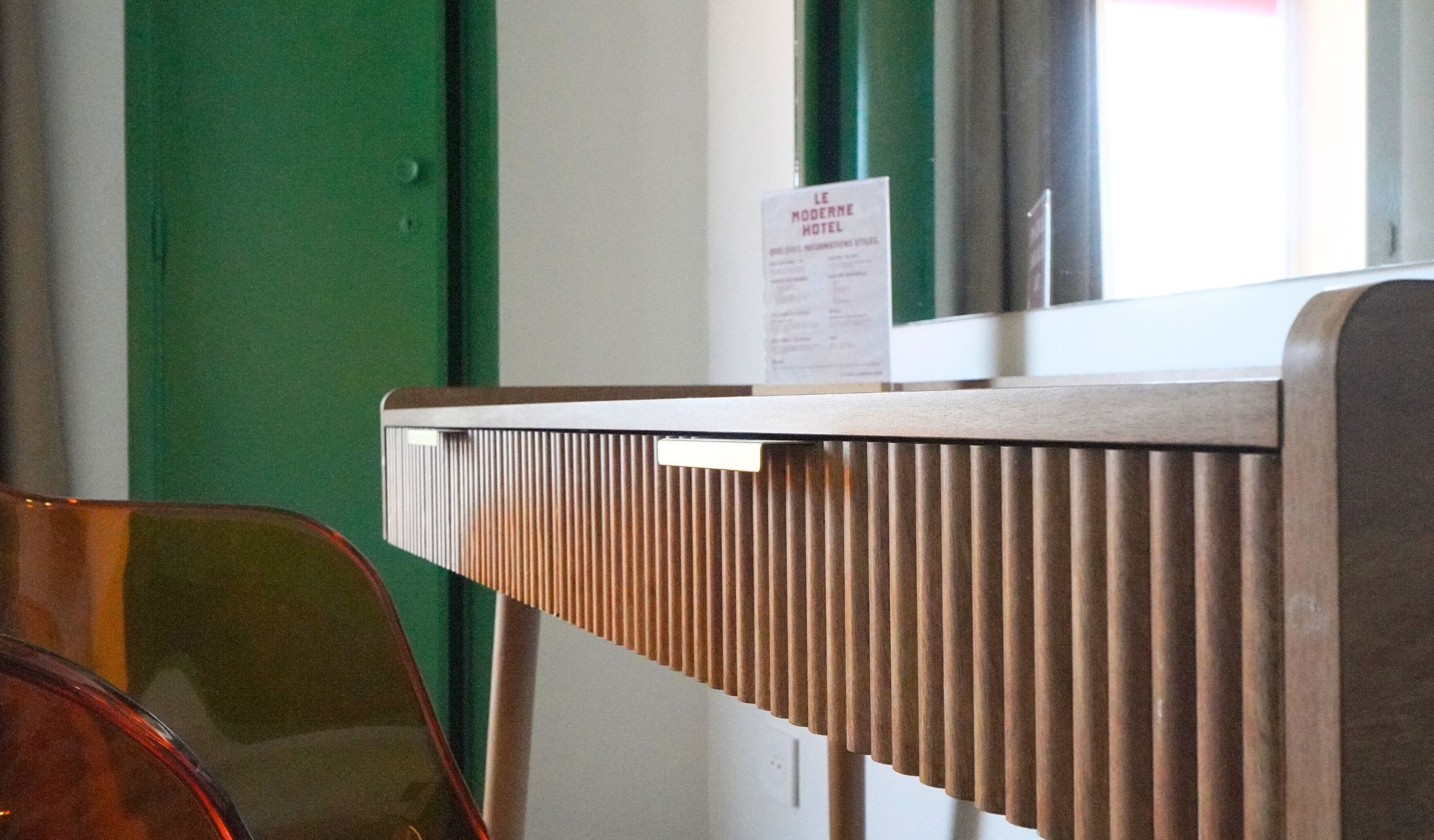 En receptionsdisk med lodrette lameller, en grøn væg og et vindue med et skilt.