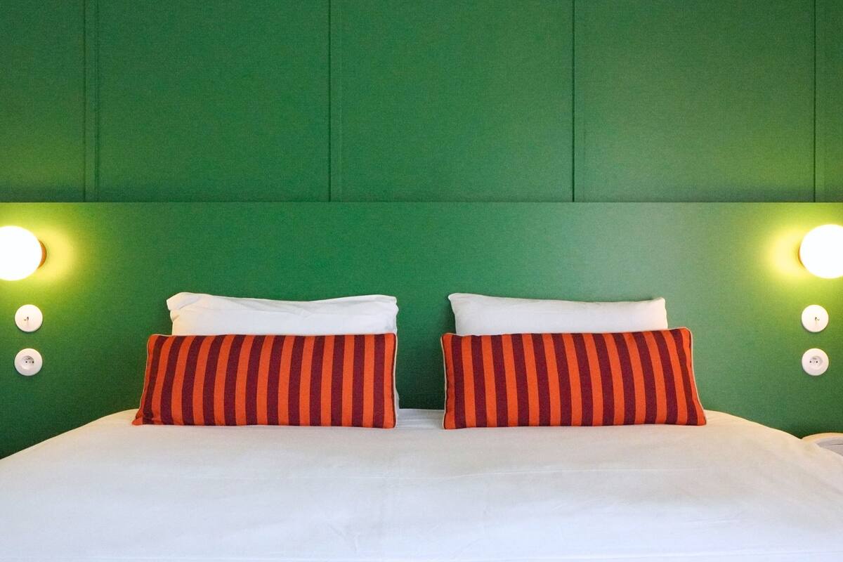 Un lit double avec deux oreillers, un mur vert et deux lampes fixées au mur.