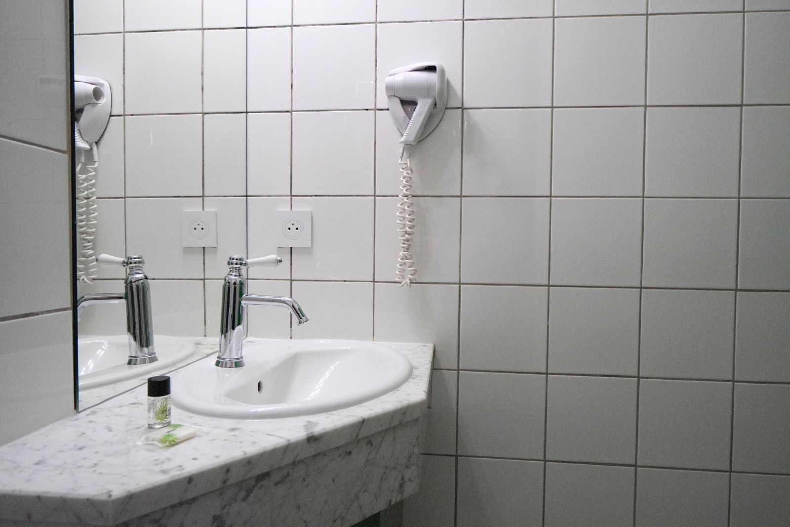 Un baño con lavamanos, dos espejos, secador de pelo y toallero.