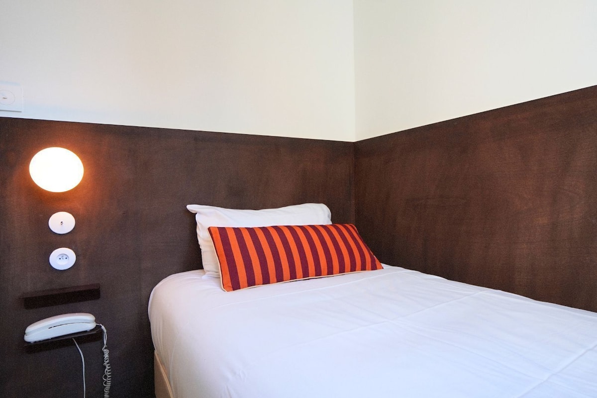 Une chambre d’hôtel avec un lit, un téléphone sur la table de chevet et un luminaire fixé au mur.