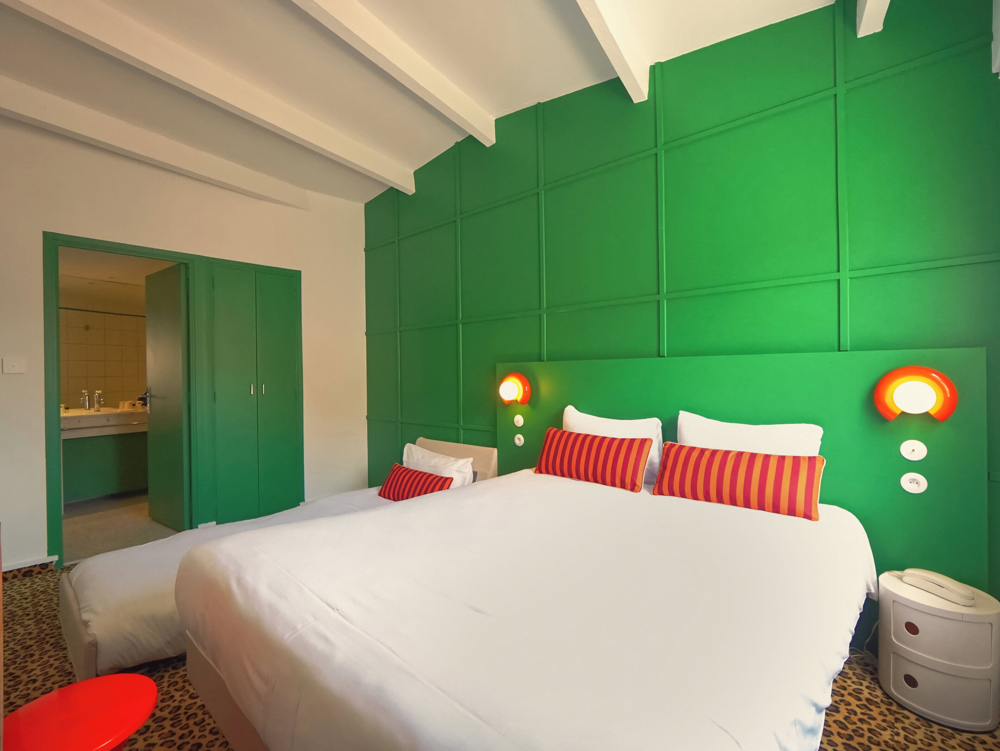 A hotel room with a large bed, a red chair, a white table, and a green accent wall.