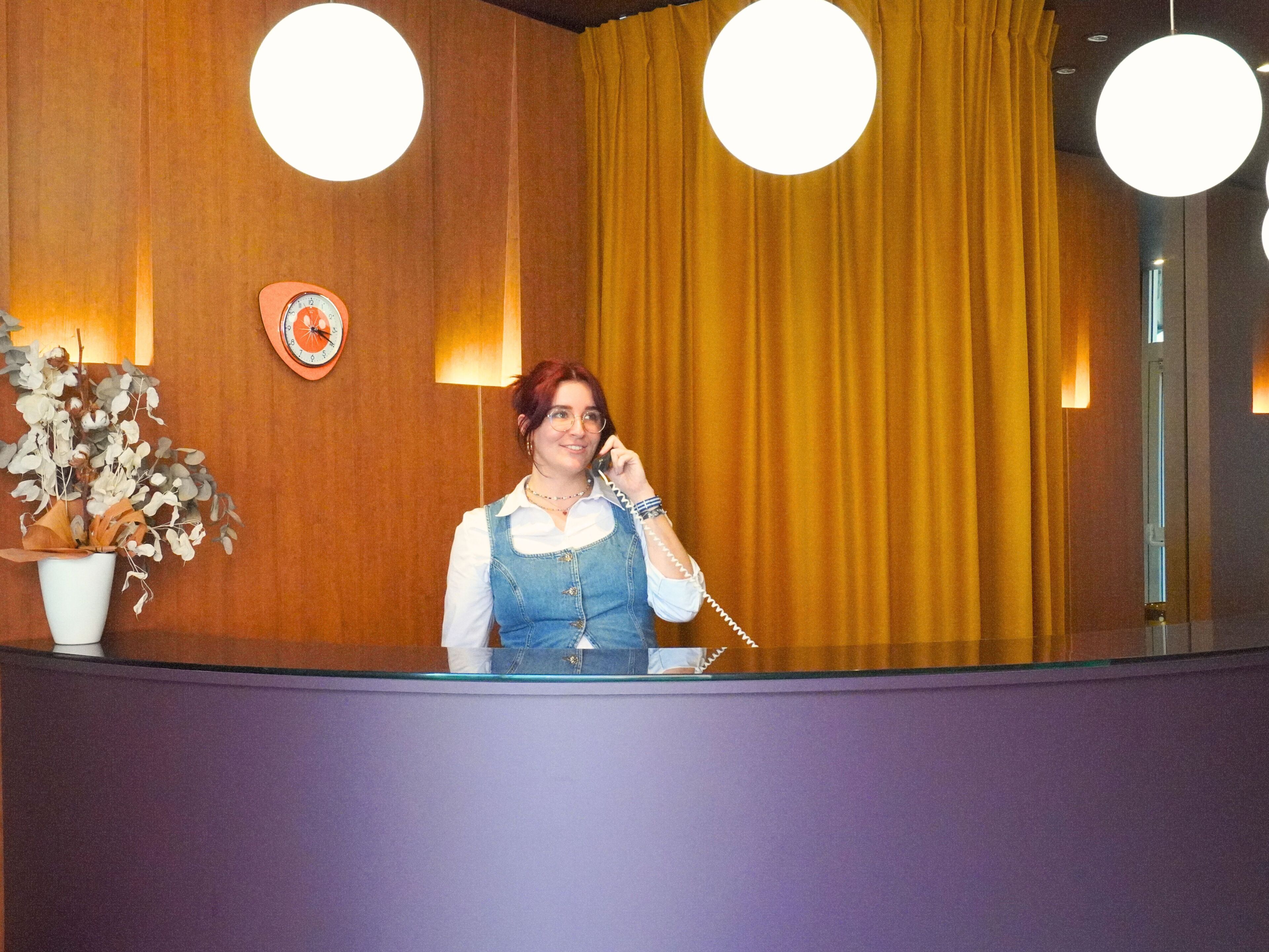 A reception area with a wooden wall, a clock, a plant, and a curtain.