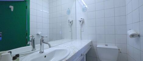 Un baño con un lavamanos blanco, dos secamanos, un inodoro y una puerta verde.