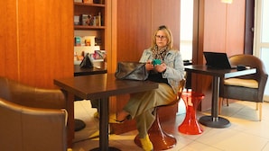 A woman sitting at a table with a laptop, surrounded by wooden walls, a bookshelf, and a red stool. - Hôtel Le Moderne (Toulouse)