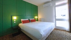 A hotel room with a green headboard, a bed with white and red striped pillows, a leopard print carpet, and a window with curtains. - Hôtel Le Moderne (Toulouse)