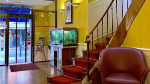 A hotel lobby with a wooden staircase, a red leather chair, and a fish tank. - Wilson Square (Toulouse)