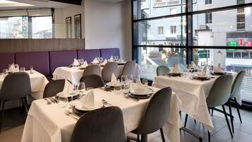 Un restaurante con mesas dispuestas para comer, amplias ventanas y vistas a la calle.