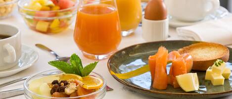 A breakfast setting with various dishes, including a bowl of fruit salad, a plate with smoked salmon and cheese, and glasses of orange juice.