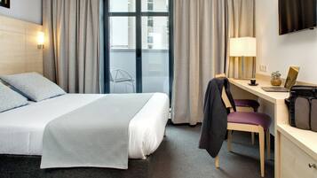 Een hotelkamer met een bed, een bureau met stoel, een lamp en een televisie aan de muur.