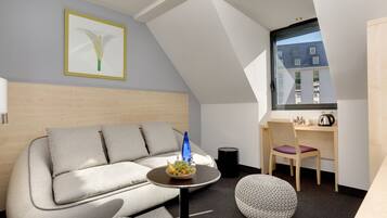 A modern room with a sofa, a small round table with a fruit bowl, a chair, and a desk with a chair.