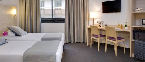A hotel room with two beds, a desk, a chair, a TV, and a luggage storage unit.