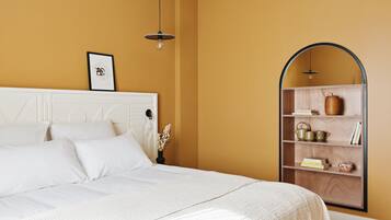 A bedroom with a white bed, a wooden shelf with books and decorative items, and a framed picture on the wall.