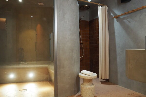 Un baño moderno con ducha envuelta en vidrio, lavamanos de mármol sobre pedestal y zona de ducha con azulejos.
