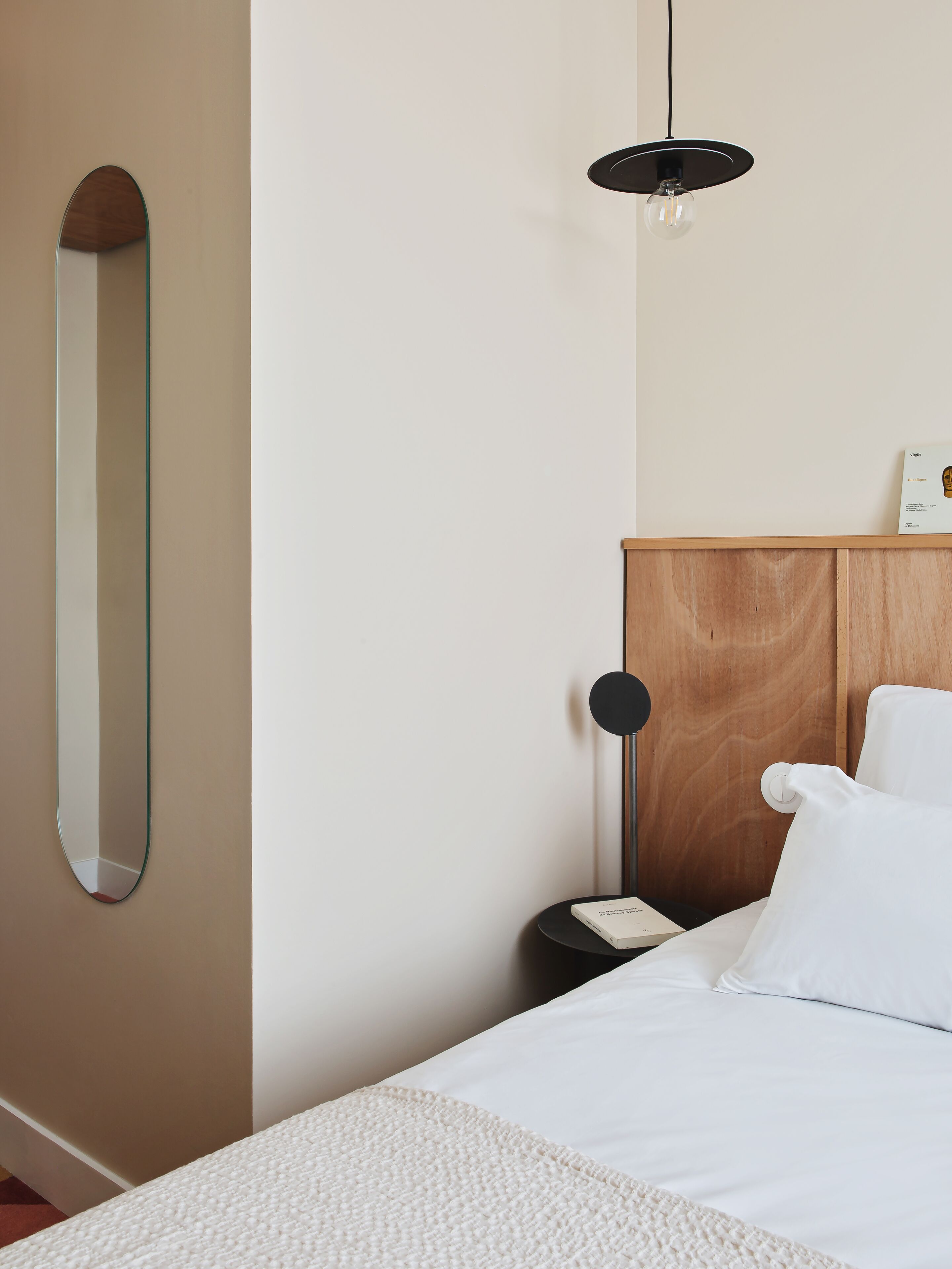 A bedroom with a bed, a bedside table, a nightstand, a lamp, a mirror, and a hanging light fixture.