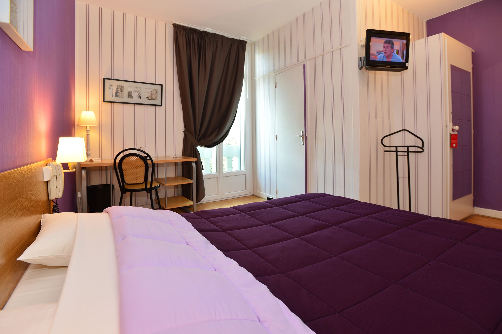 Una habitación de hotel con cama, escritorio, silla, televisor y armario.
