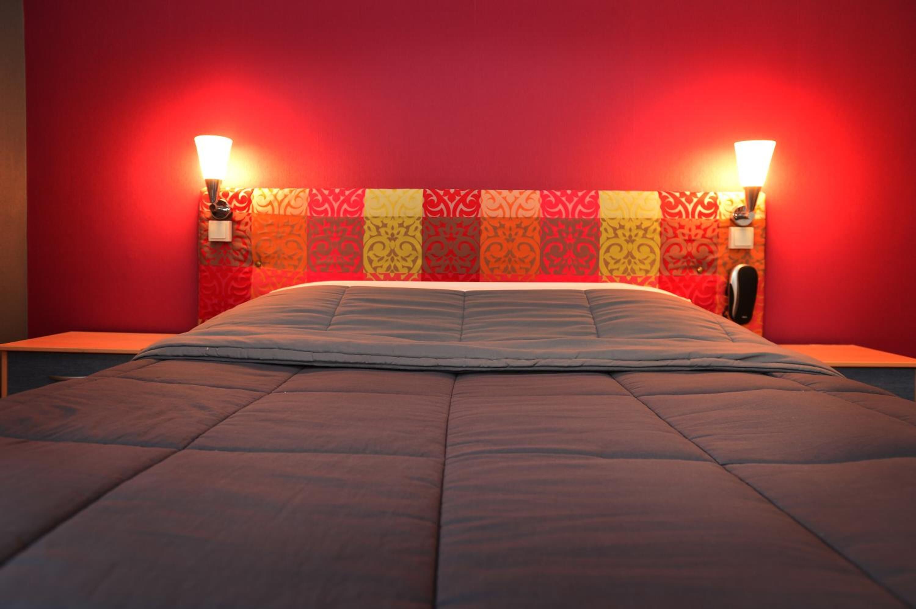 Un lit avec une tête de lit à motifs, deux lampes de chevet et un mur rouge.