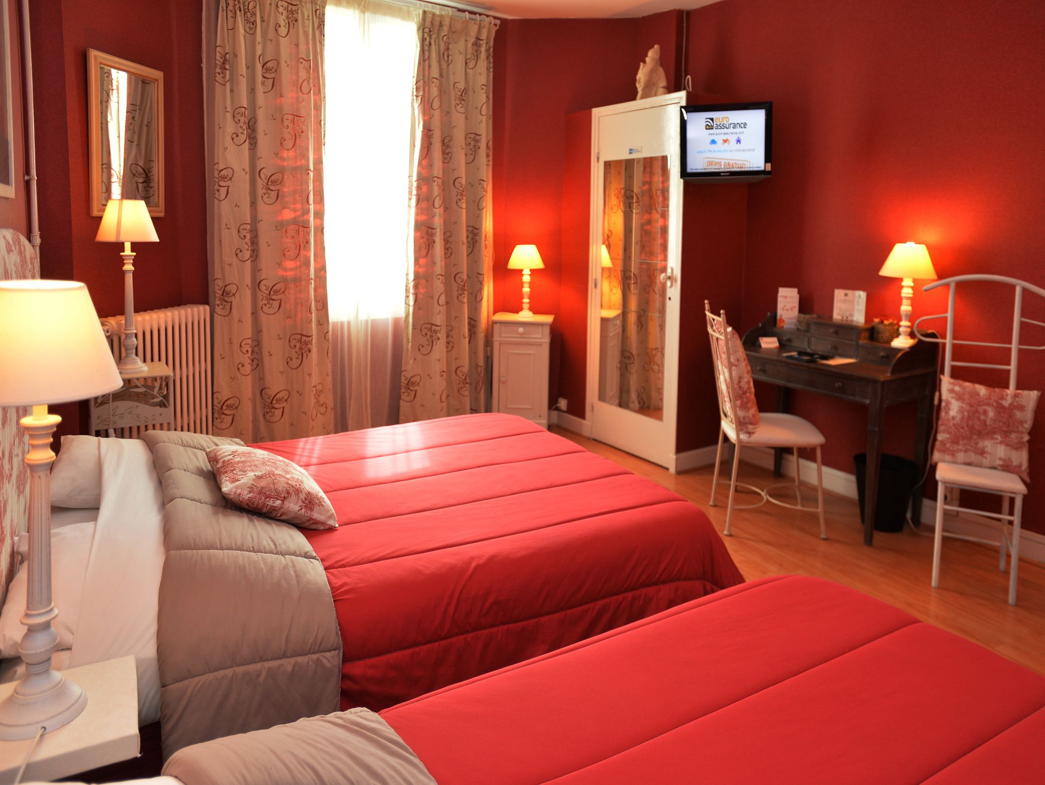 Camera d'albergo con due letti, una scrivania, una sedia, un televisore e un termosifone.