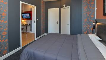 Un dormitorio con una cama grande, dos puertas, un televisor en la habitación contigua y un papel tapiz con estampado.