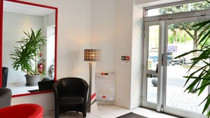 A hotel reception area with a large mirror, a potted plant, a black chair, a floor lamp, and a glass door leading outside. - La Croix Blanche (Tarbes)