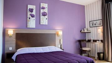 A bedroom with a large bed, a desk, and a chair. There are two wall-mounted lamps and a telephone.