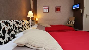 A hotel room with a cow print headboard, two red beds, a television on the wall, and a chair with a patterned cushion.