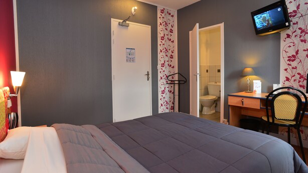 A bedroom with a bed, a desk, a chair, a TV, and a bathroom door. - La Croix Blanche (Tarbes)