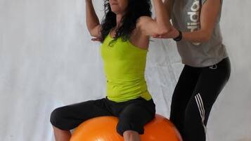 Una persona haciendo ejercicio sobre una pelota de entrenamiento naranja, con un entrenador.