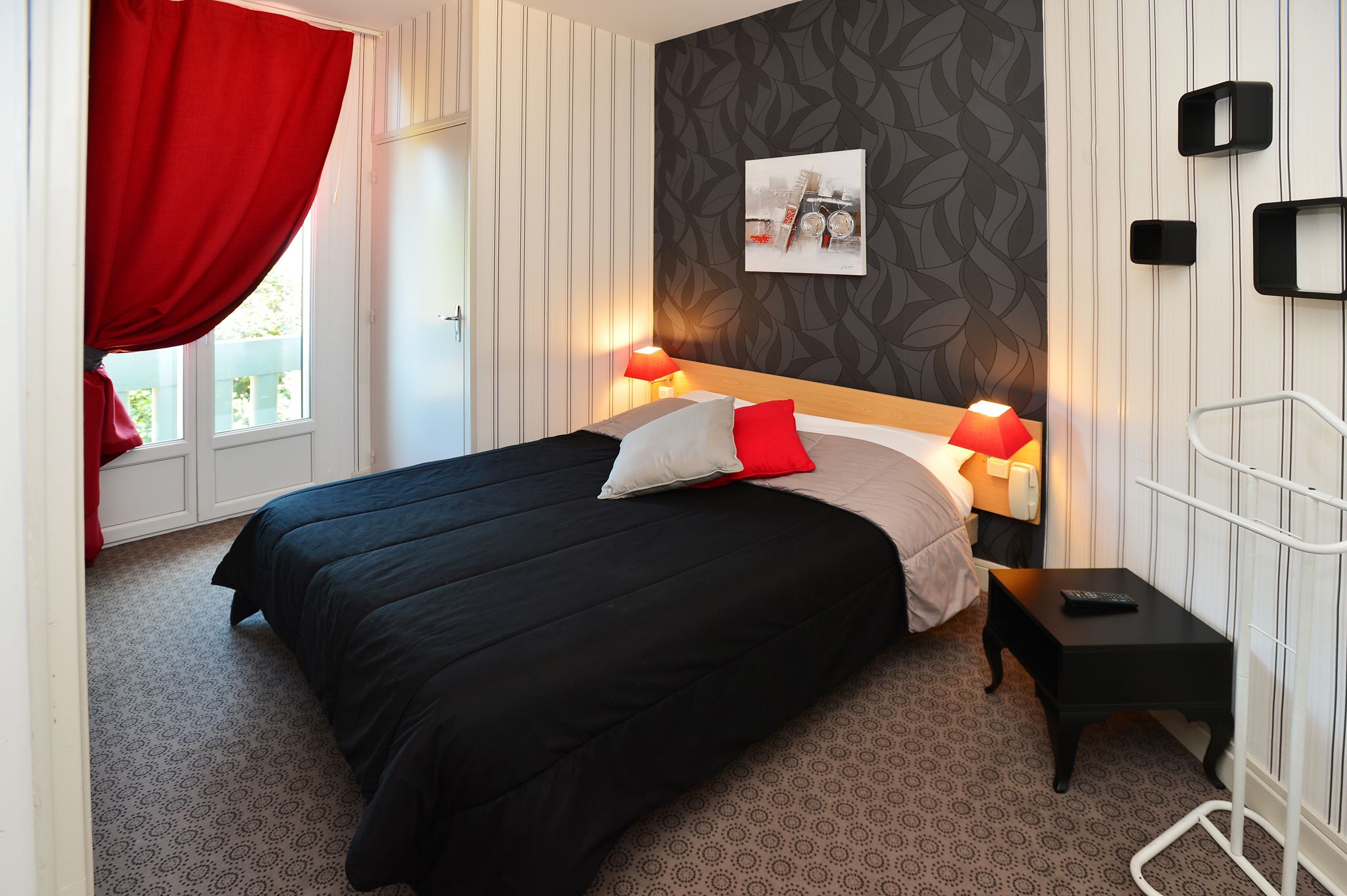 Una camera da letto con un letto, lampade da comodino, un comodino, una finestra con tende e un quadro appeso al muro.