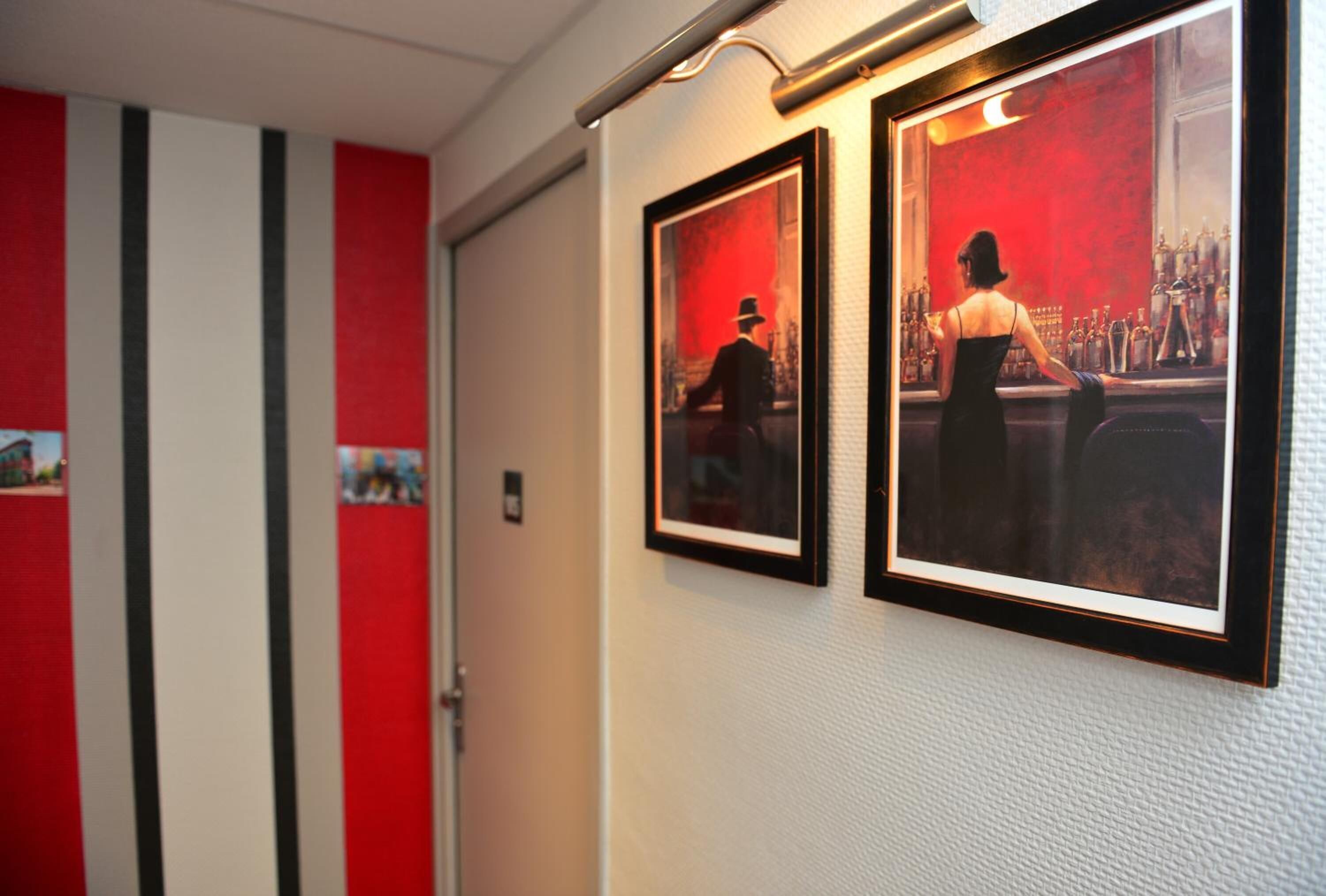 A hallway with red and white striped walls, two framed pictures on the wall, and a door at the end.