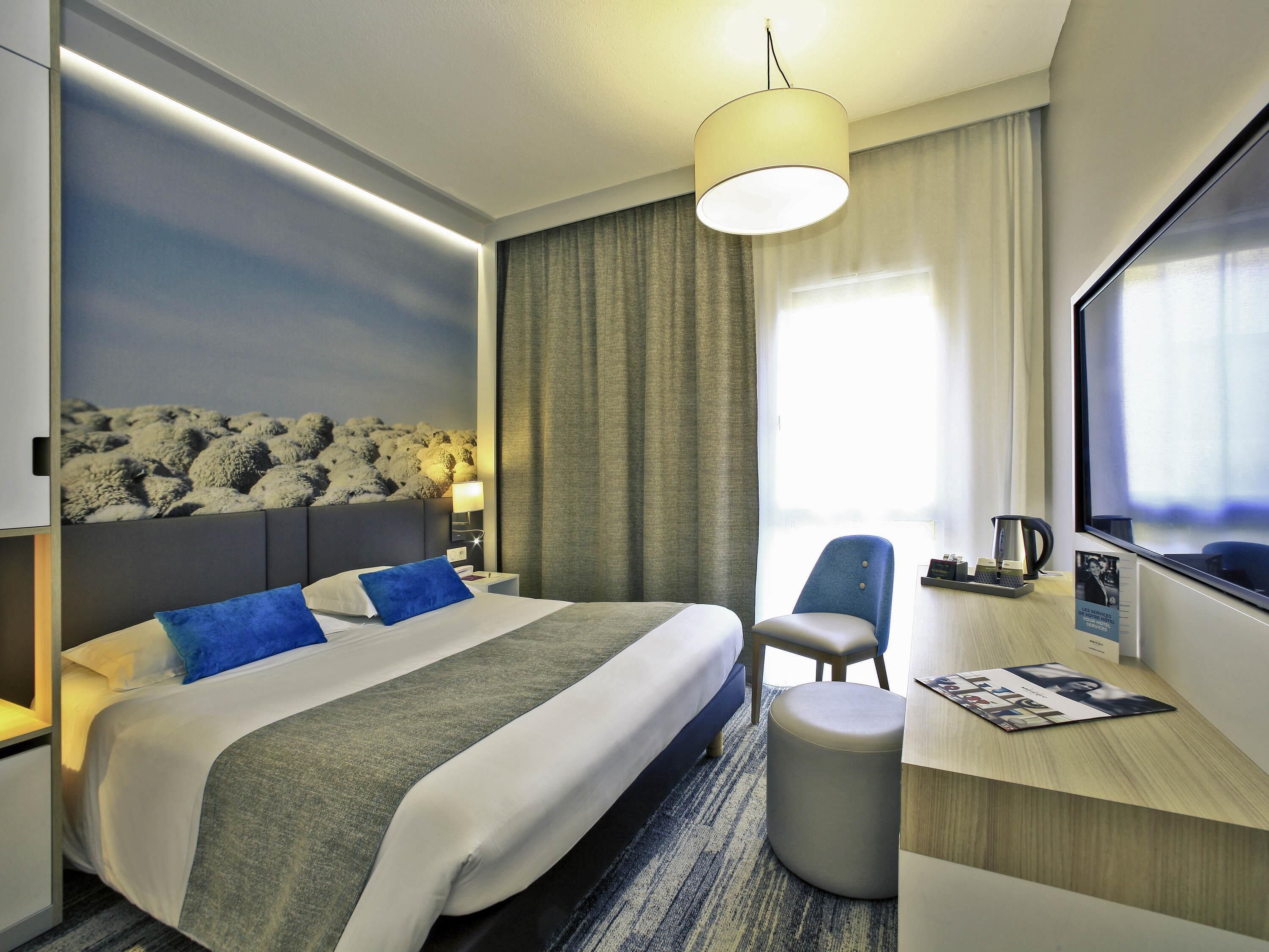 A hotel room with a bed, a desk, a chair, a lamp, and a large window.