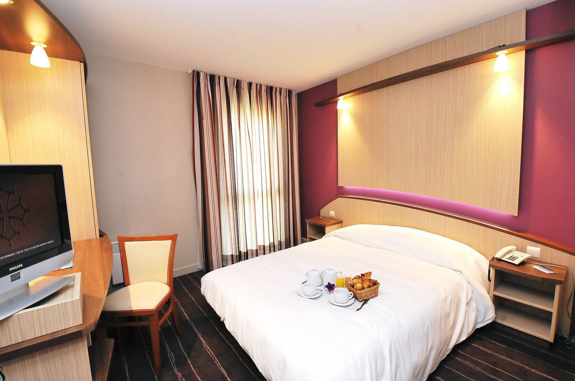 Une chambre d’hôtel équipée d’un lit, d’une télévision, d’un bureau avec une chaise, d’une table de chevet et d’un téléphone.