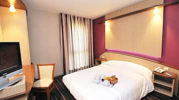 Une chambre d’hôtel équipée d’un lit, d’une télévision, d’un bureau avec une chaise, d’une table de chevet et d’un téléphone.