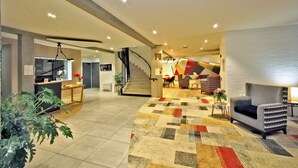 A modern hotel lobby with a staircase, a reception desk, and a seating area. - Hôtel Mercure Castres L'Occitan (Castres)