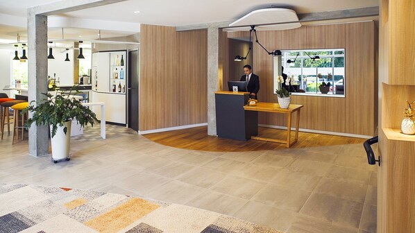 A modern reception area with a wooden reception desk, a potted plant, and a large window with a view of the outdoors.